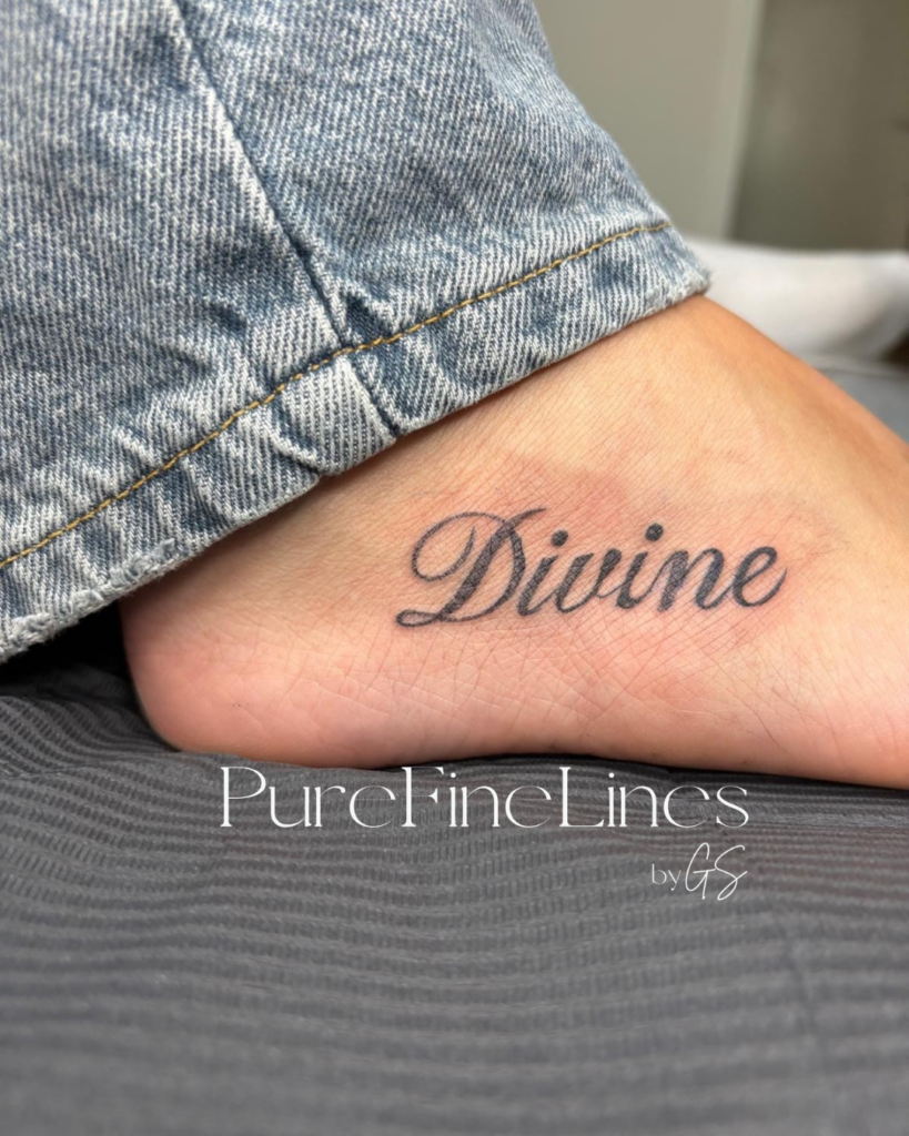 Fineline Schriftzug-Tattoo „Divine“ in Schreibschrift am Fußrücken, gestochen bei PureFineLines by GS