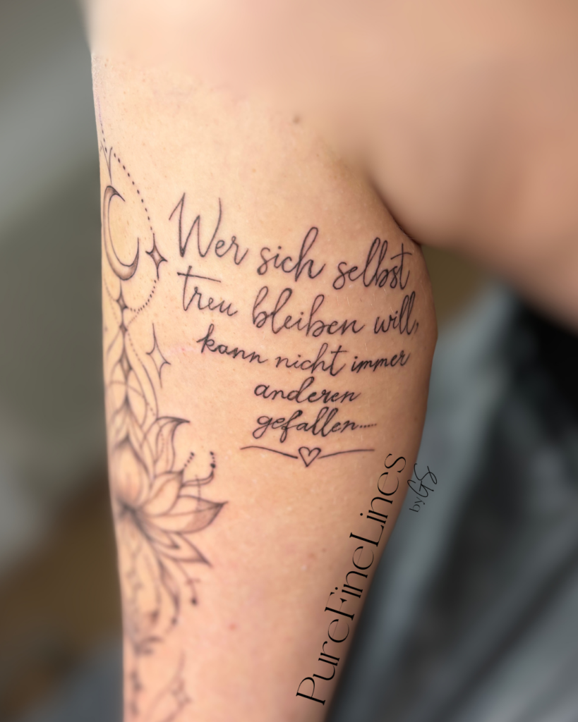 Fineline Tattoo am Oberarm mit Spruch in Schreibschrift, Mond und floralen Elementen, PureFineLines by GS