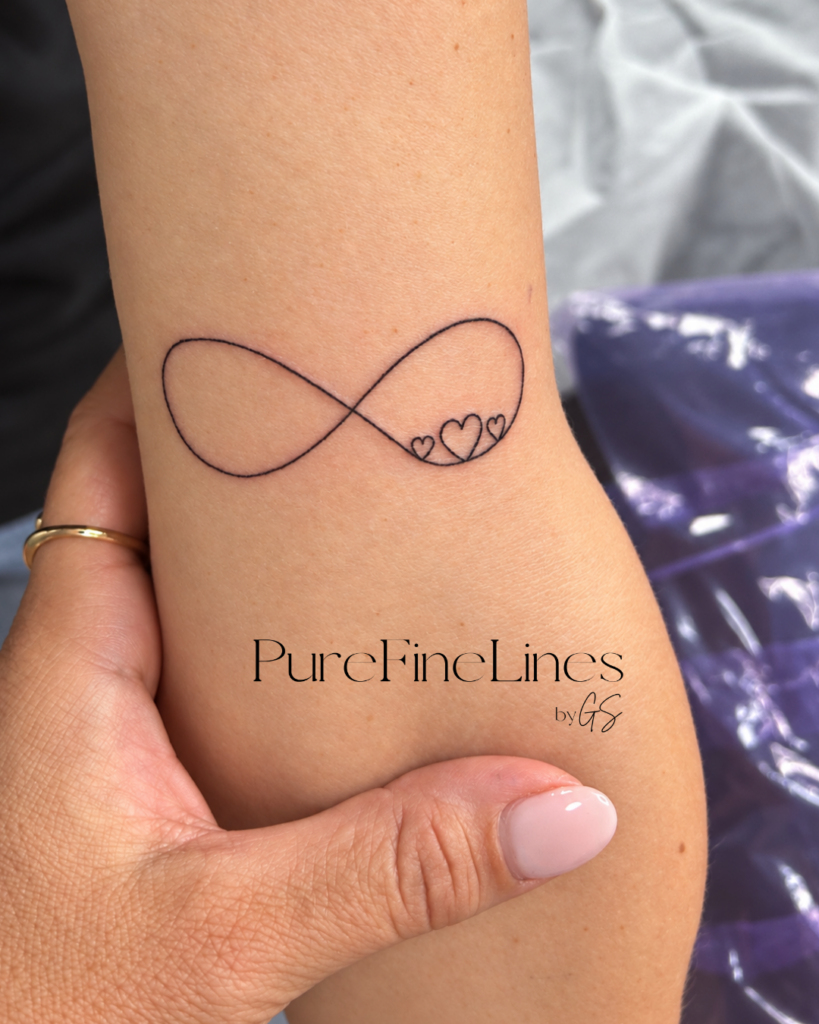 Fineline Tattoo Unendlichkeitszeichen mit zwei kleinen Herzen am Unterarm, gestochen bei PureFineLines by GS